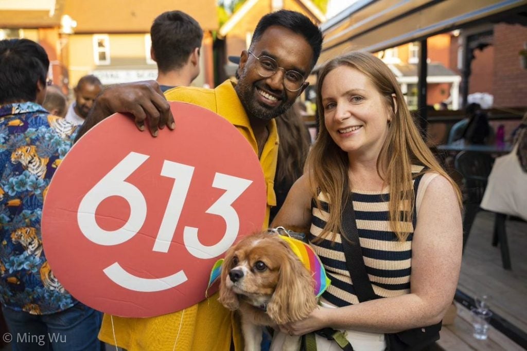 Man holding a 613 cardboard cutout standing next to a women holding a dog.