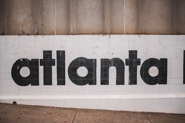 Black text spelling 'atlanta' in lowercase letters on a white wall with beige concrete above